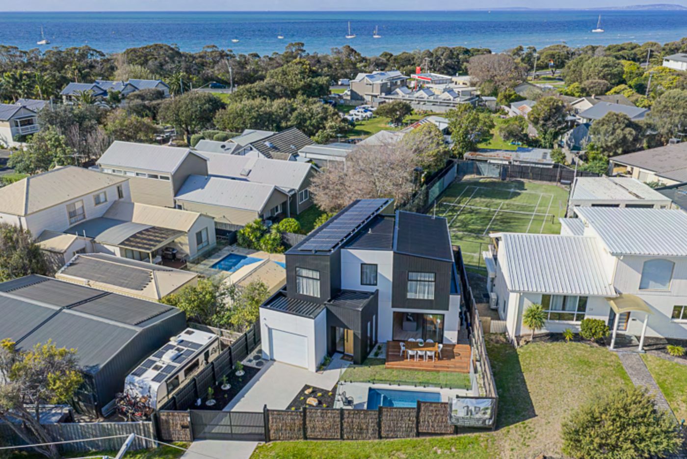 Aerial view of Casa al Mare with its pool and deck, the tennis court next door and Port Phillip Bay in the distance
